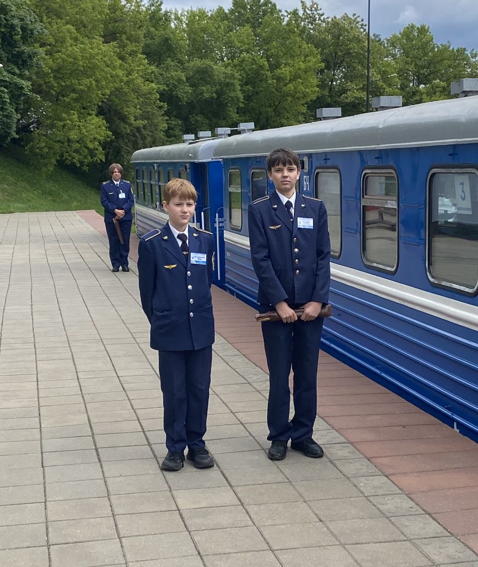 Дети в форме железнодорожников стоят к вагона поезда детской железной дороги